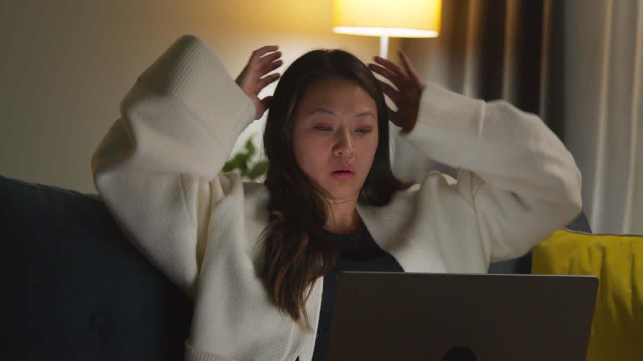 스트레스를 받고 불안한 여성은 집에서 저녁을 보내고 소파에 앉아 인터넷이나 소셜 미디어 뉴스 또는 노트북에서 금융 이야기에 반응합니다.