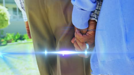 Animation-of-light-moving-over-midsection-of-senior-couple-walking-holding-hands