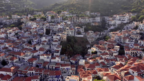 Aerial:-Backwards-reveal-shot-of-Skopelos-town-in-Skopelos-island-in-Aegean-Sea,-Greece-during-sunset