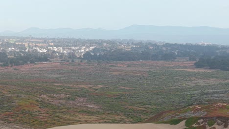 sweeping aerial view captures fort ord beach’s sandy stretches with highway 1 winding through distant hills.