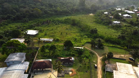 Suburban-houses-and-mopeds-on-a-road,-sunset-in-Ebolowa,-Cameroon---Aerial-view