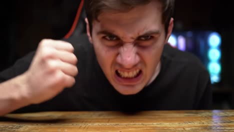 intense emotion displayed: a young person exhibits frustration and anger during a moment of tension, gripping the table with a clenched fist in a dimly lit room