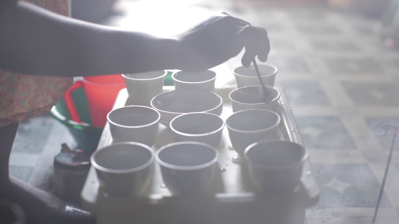 mujer africana revuelve tazas de café en bandeja, vapor y humo de incienso