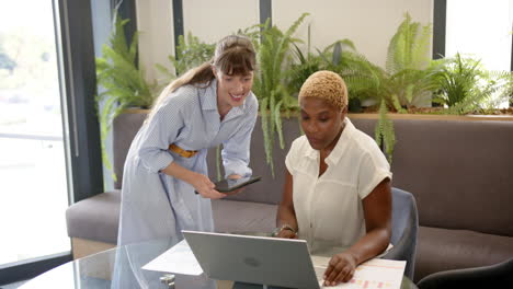 collaborating in office, two women using laptop and tablet for project work