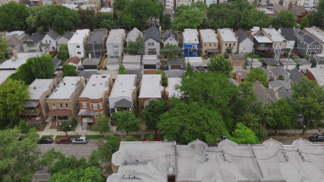 Lavtflyvende drone-udsigt over en boliggade i Chicago med murstenshuse, tage, parkerede biler og fuldvoksne træer