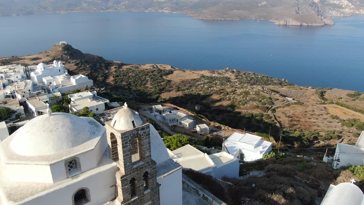 vista de avión no tripulado en grecia volando sobre una iglesia blanca en una colina con una casa blanca griega ciudad frente al mar azul en una montaña