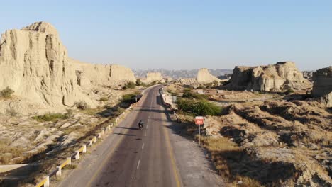 aerial tracking shot behind motorbike driving along empty highway road through hingol national park in balochistan desert landscape