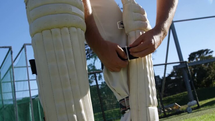 Giocatore di cricket che allaccia i parastinchi da battuta durante una sessione di allenamento