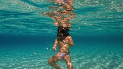 Under-water-scene-of-a-cute-little-girl-with-diving-mask-surrounded-by-hungy-fish-feeding-them-with-bread