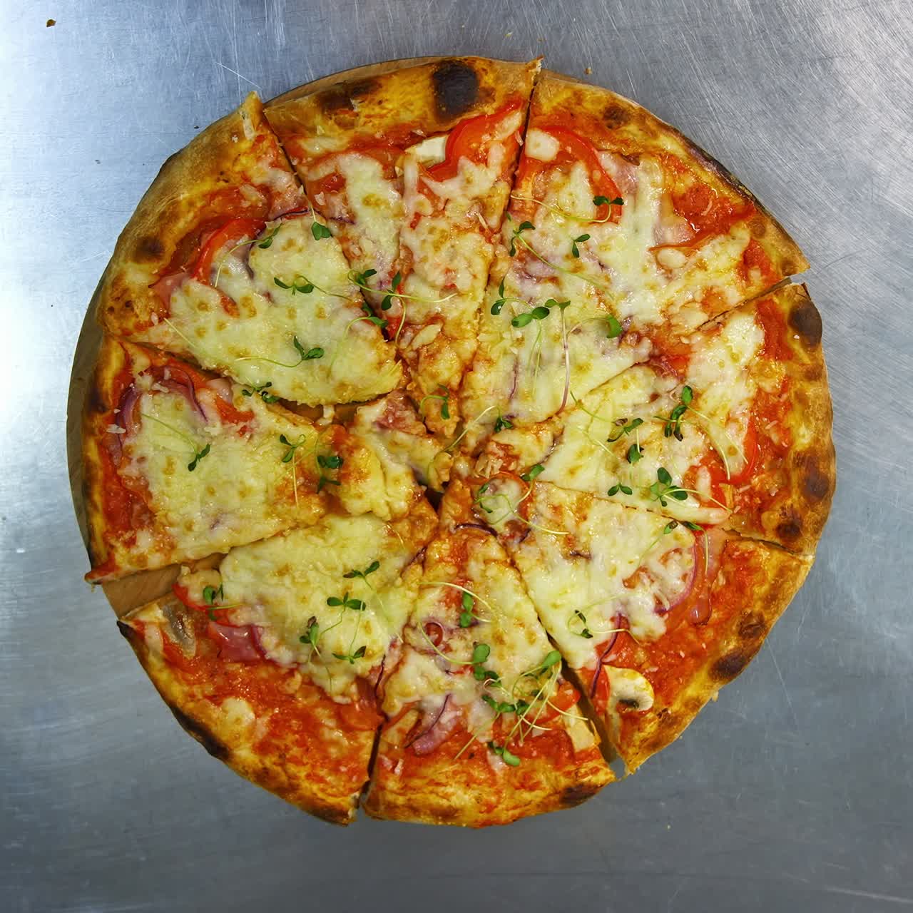 Pizza preparata al momento su un tavolo in acciaio inossidabile in una cucina bar. Pizza calda appetitosa con formaggio, pancetta e verdure sulla parte superiore