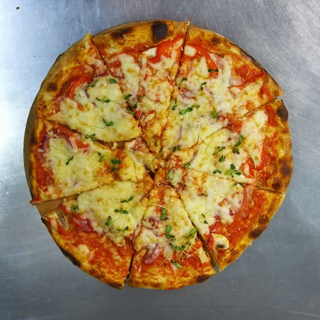 freshly prepared pizza on a stainless steel table in a cafe kitchen. appetizing hot pizza with cheese, bacon and greens on the top
