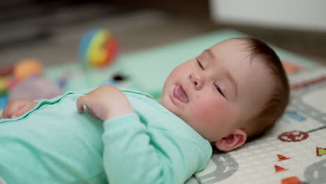 lovely boy lying peacefully on the bed shows tongue and turns his head away. little baby resting indoors. close up. blurred backdrop.