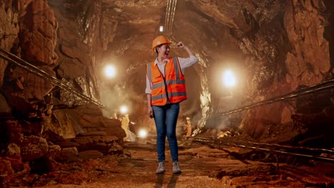 full body of asian female engineer with safety helmet flexing her bicep and smiling to camera in underground mine tunnel