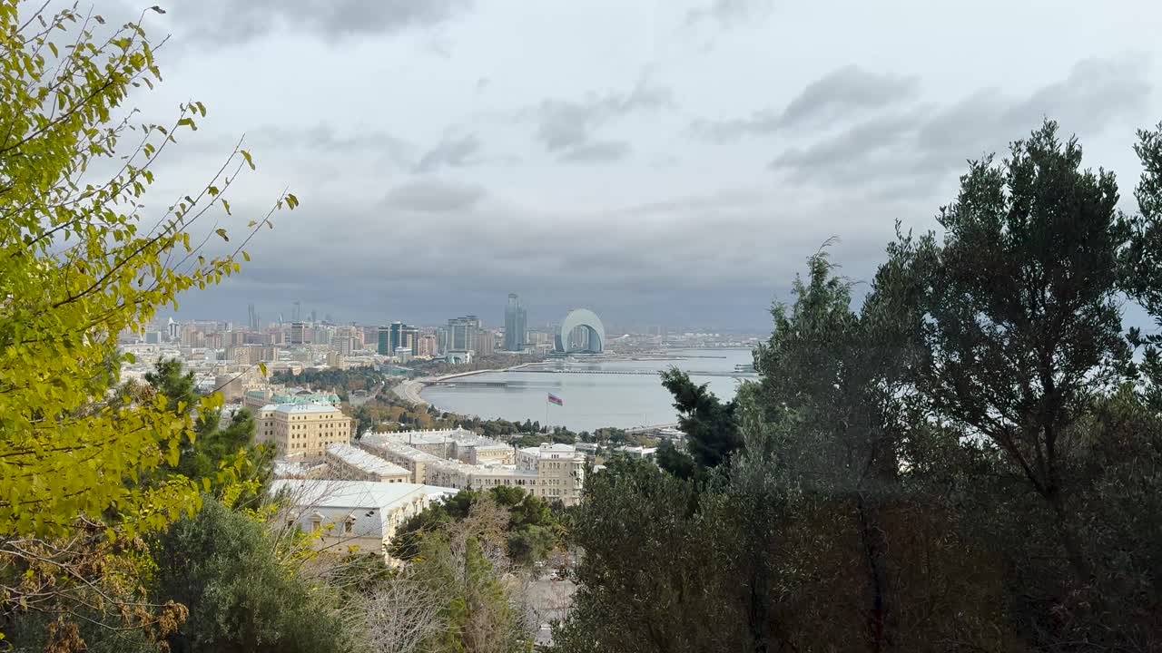 Panoramic view of Baku’s waterfront skyline framed by trees on a cloudy day. Azerbaijan