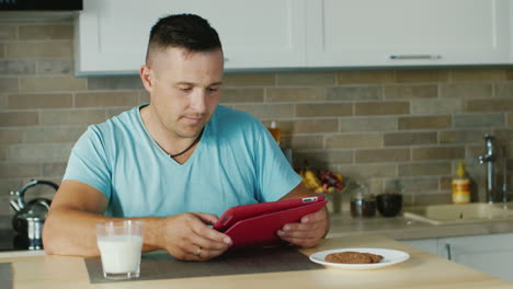 a young man uses tablet in the kitchen standing next to a glass of milk healthy lifestyle