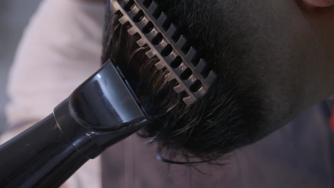 Black brush comb and black hair dryer used to comb straighten black hair on top of black head by barber, filmed in closeup shot in vertical handheld slow motion style