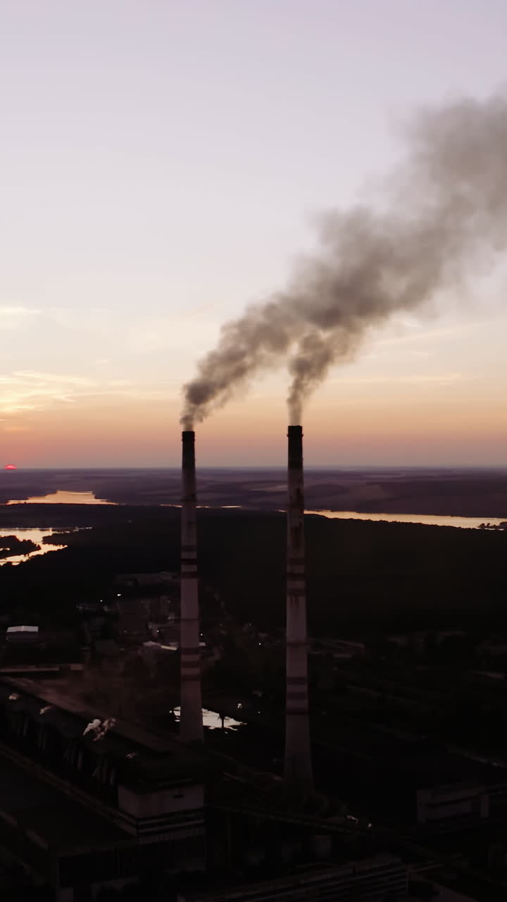 Industrial factory near the river. Harmful smoke comes into the air in the evening. Metallurgical plant produce chemical smoke through pipes. Vertical video