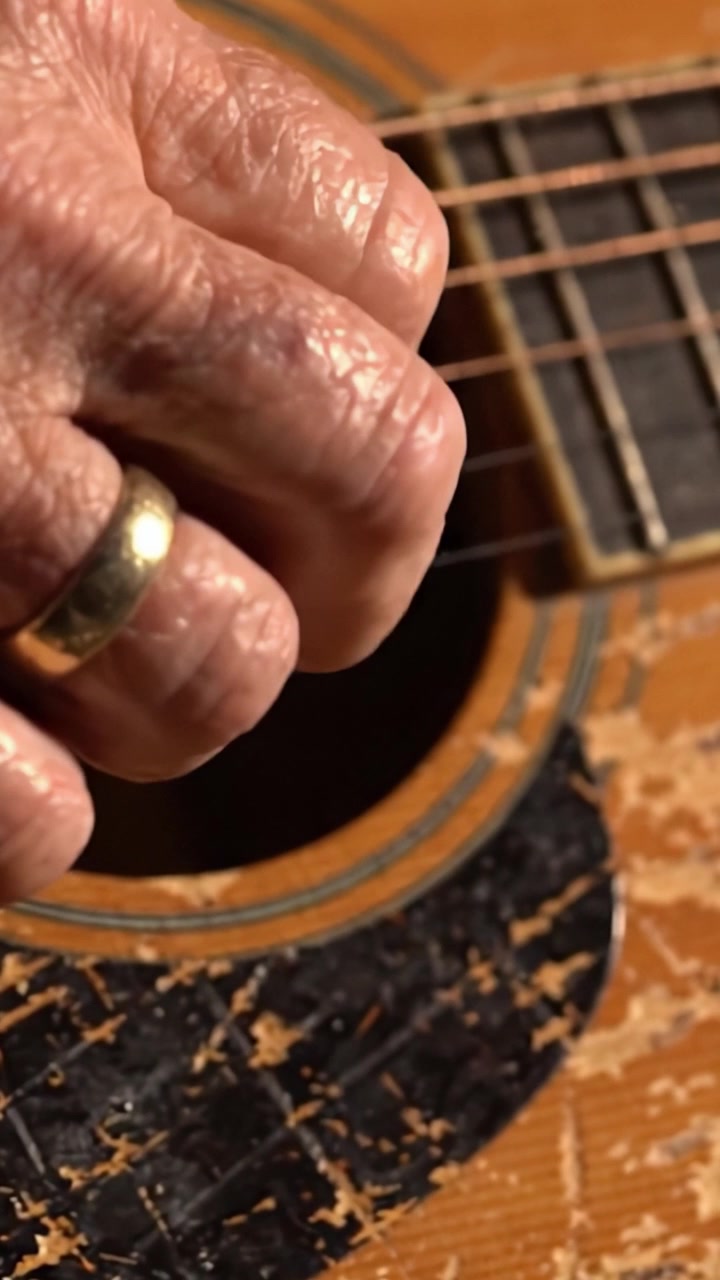 Un primo piano di una mano callosa che strimpella una chitarra acustica, dimostrando la passione e l'abilità di un musicista esperto.