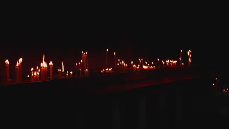 las velas de cera se queman en la oscuridad en la iglesia contra el fondo oscuro, cámara lenta