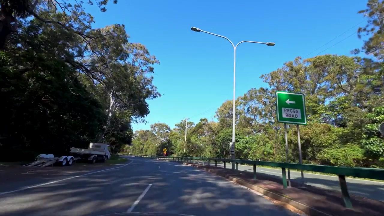 Vue à la première personne conduisant le long d'une route pavée bordée d'eucalyptus sous un ciel bleu clair.