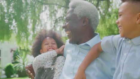 Loving-Grandfather-Talking-With-Grandchildren-In-Garden-At-Home