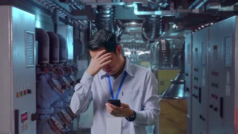 asian male professional worker standing with his smartphone in engine control room, he is nodding his head with dissapionted