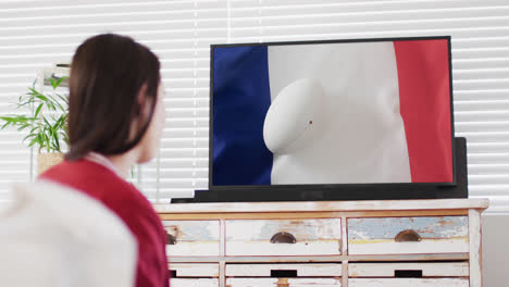 Mujer-Caucásica-Viendo-La-Televisión-Con-Una-Pelota-De-Rugby-En-La-Bandera-De-Francia-En-La-Pantalla.