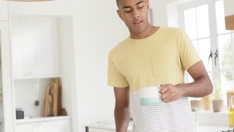 hombre biracial feliz bebiendo café en una cocina brillante, en cámara lenta