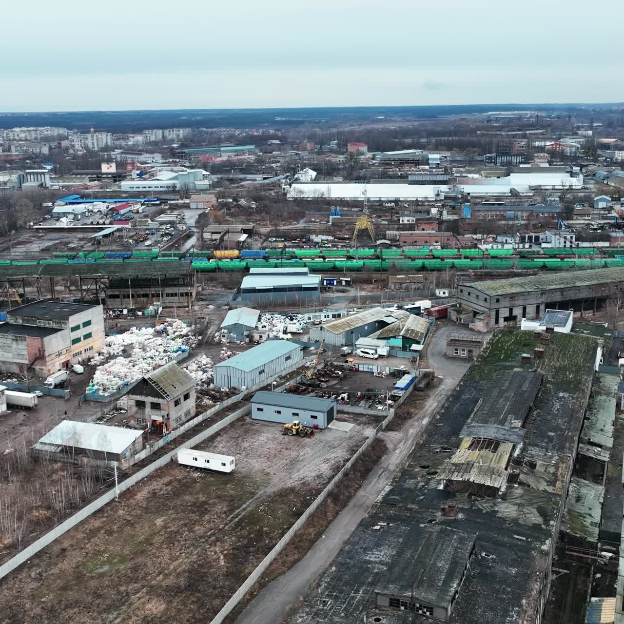 Huge industrial territory abandoned long ago. Aerial view of old ruined warehouses near railways and trains. City view at the backdrop