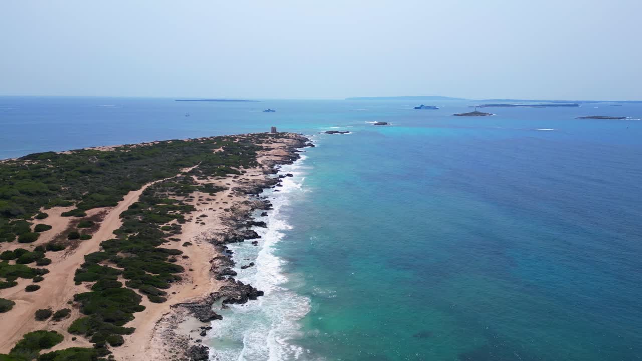 Turquoise waves crashing on the rocky coast of Ses Salines beach with the ancient watchtower. Majestic aerial view flight panorama overview drone