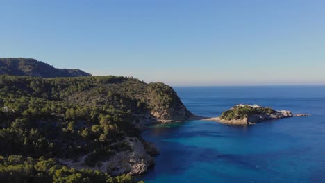 Drone-flying-forward-over-small-bay-on-Ibiza