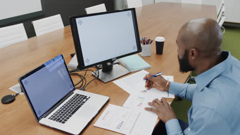 Afroamerikanischer-Geschäftsmann-Im-Büro-Mit-Computer-Und-Laptop,-Kopierplatz-Auf-Bildschirmen,-Zeitlupe