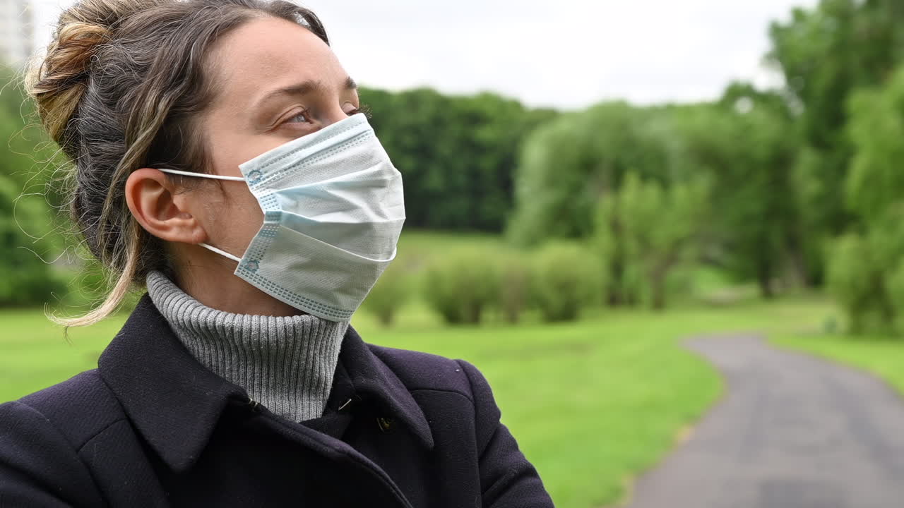 Woman putting on a medical face mask while standing in a park