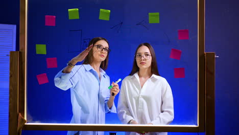 creative team brainstorm sesh. two women engage in a brainstorming session using sticky notes on a clear board in a vibrant workspace
