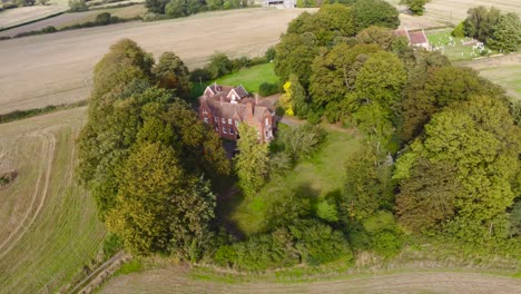 aerial: agricultural farm land with house, tree and cemetery at suffolk, england - drone flying rotation shot