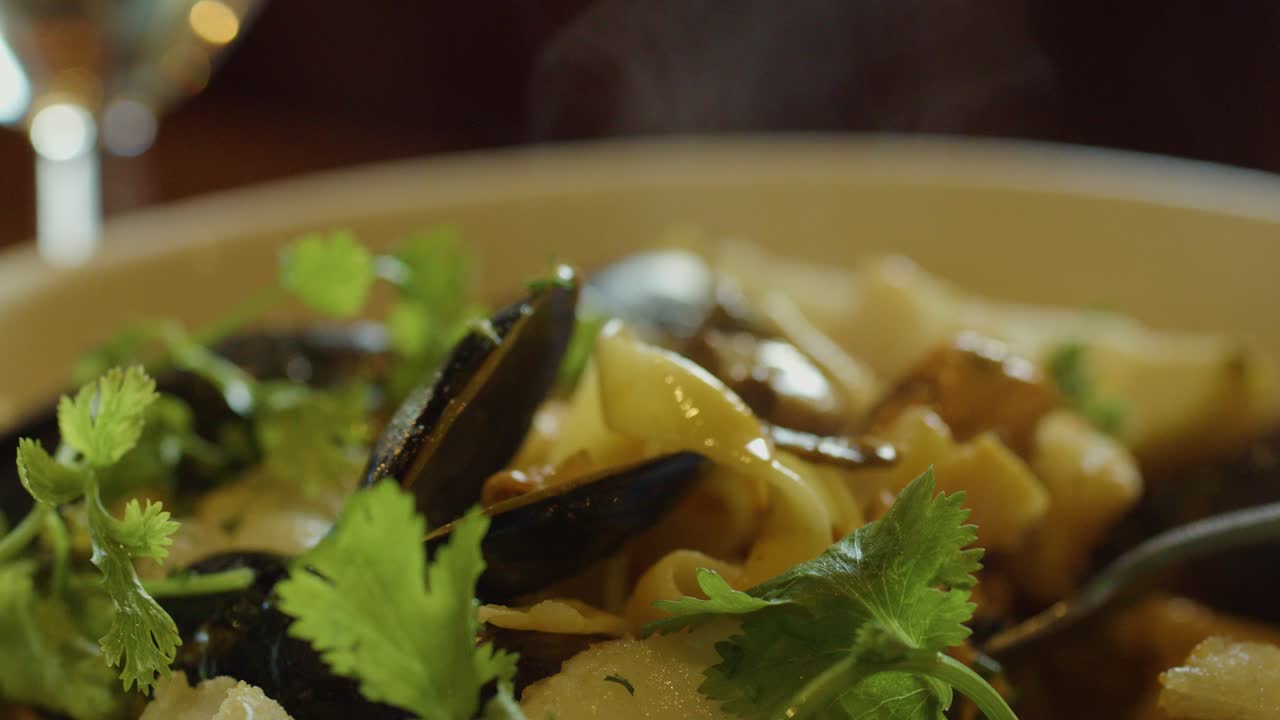 A close-up, macro view of hot seafood chowder with mussels, fish, squid, and scallops, garnished with fresh herbs, served in warm ambient lighting