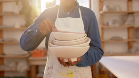 Mid-section-of-african-american-potter-holding-bowls-in-pottery-studio,-slow-motion