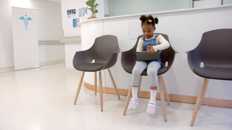 African-american-girl-sitting-in-hospital-waiting-room-and-using-tablet,-slow-motion