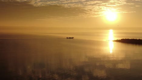 Single-fishing-boat-sits-calmly-on-open-waters,-serene-peaceful-reflection-of-yellow-sky