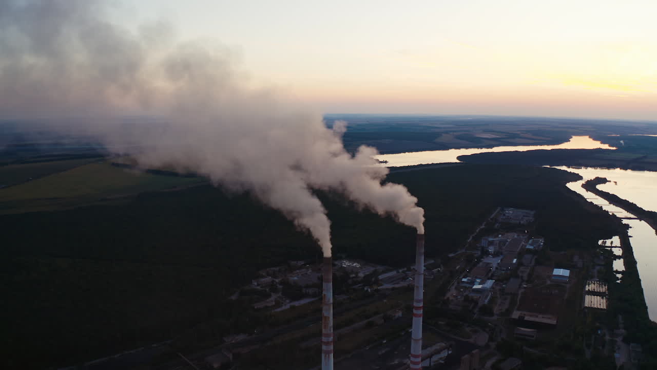 White smoke from pipes in the natural environment. Industrial factory near the beautiful river in the countryside in the evening. Air pollution.