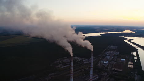 white smoke from pipes in the natural environment. industrial factory near the beautiful river in the countryside in the evening. air pollution.