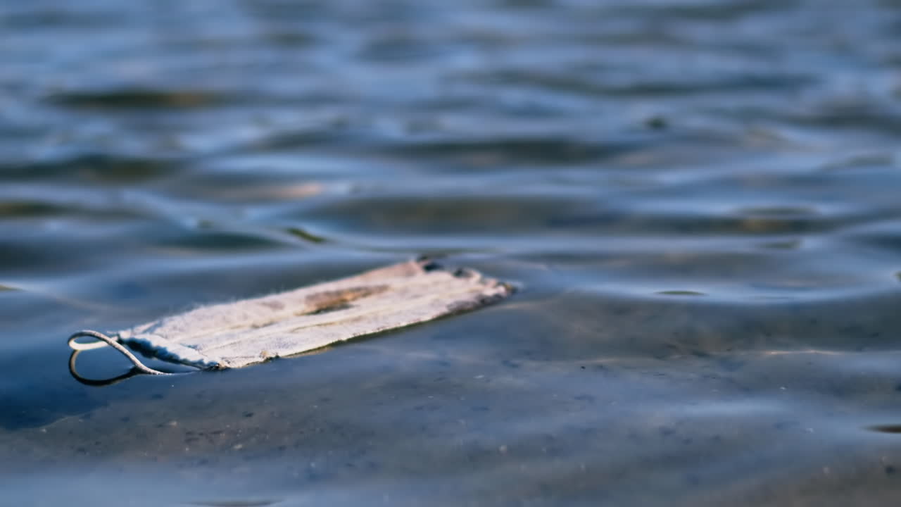 Dirty medical mask floating floating on water. Pollution idea