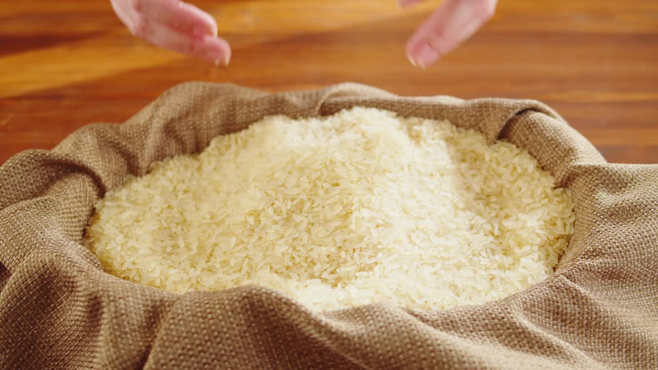 Hands scooping raw rice from a burlap sack