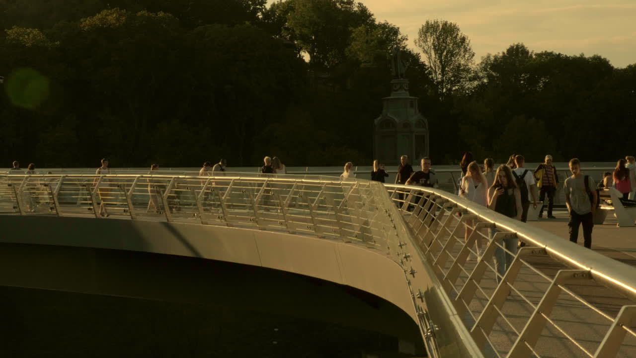 Backlit wide shot of people walking across the glass bridge in Kiev on a warm autumn evening