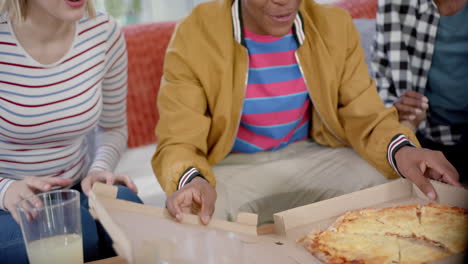 Happy-diverse-group-of-teenage-friends-sitting-on-couch-and-eating-pizza-at-home,-slow-motion