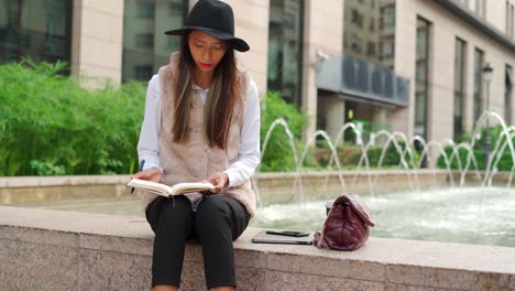 hispanic woman taking notes near fountain