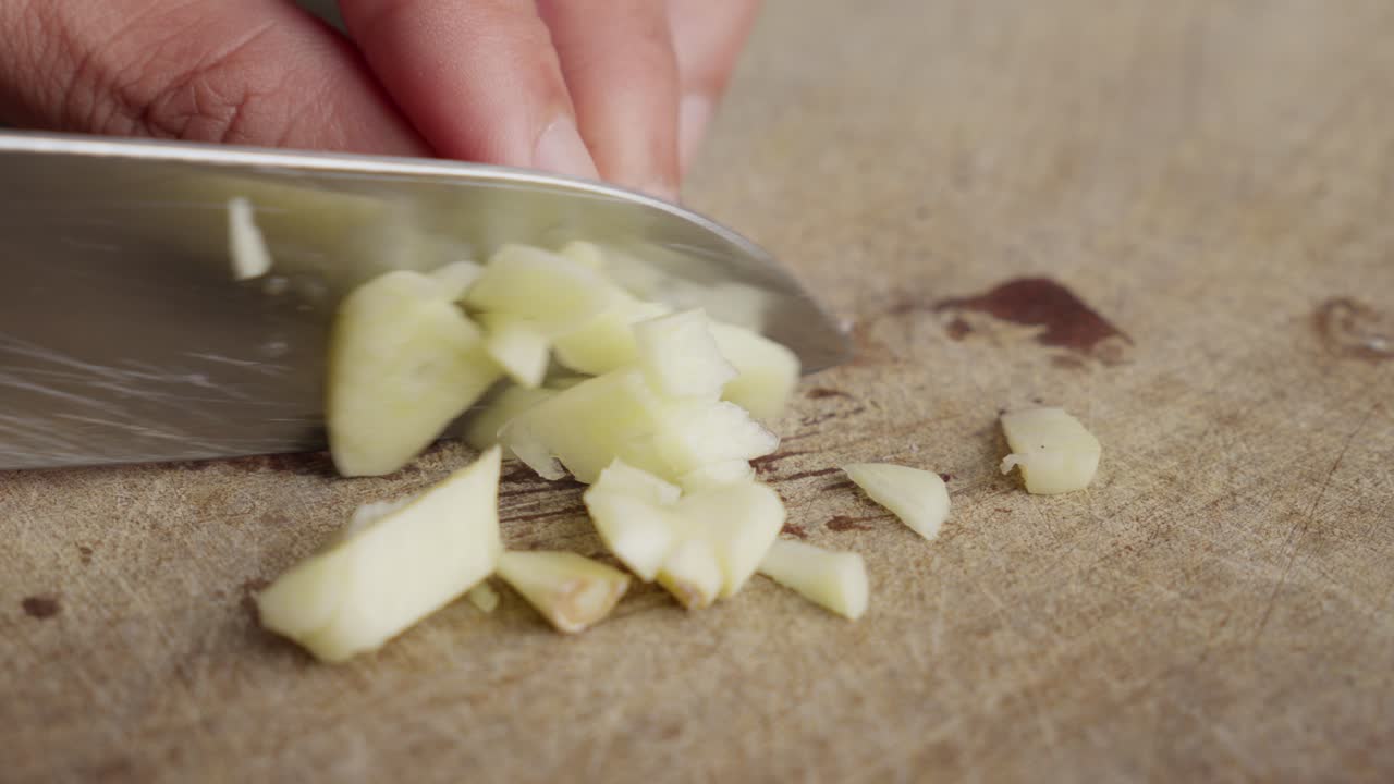 Close Up Of Hands Chopping A Raw Clove Of Garlic Into Small Pieces.