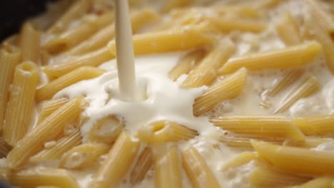 Anonymous-cook-adding-cream-into-frying-pan-with-macaroni