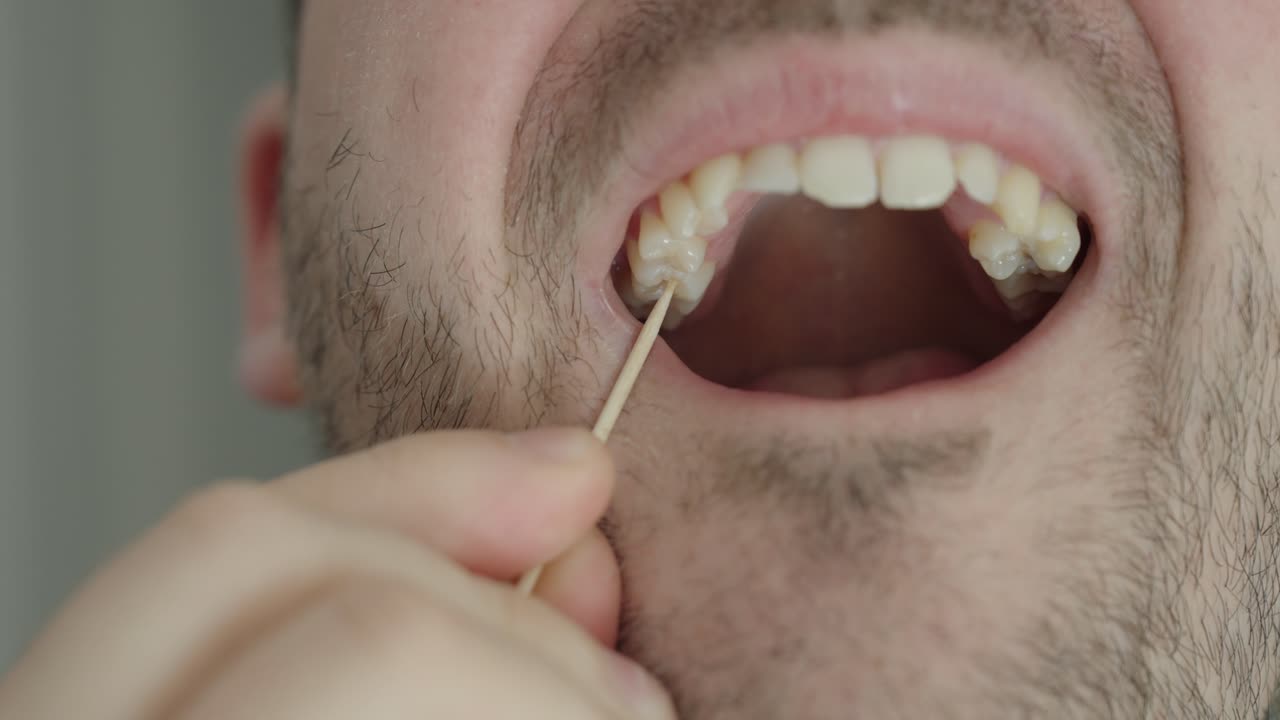 Primo piano di un uomo che rimuove il cibo dai denti con uno stuzzicadenti. Concetto di igiene orale, cura dentale e routine quotidiana di salute.