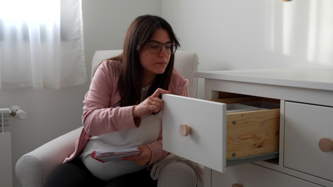 Pregnant woman opening the dresser drawers of baby's room and checking them